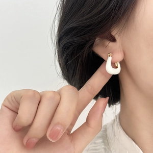 Boucles d'oreilles dorées en U avec émail blanc portées par un mannequin femme