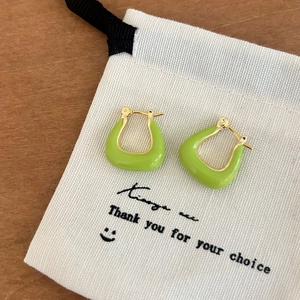 Détail des boucles d'oreilles émaillées vert herbe en forme de U sur sac en toile