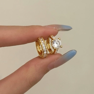 Close-up of gold hoop earrings set with zircon stones held between fingers