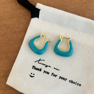 Détail de boucles d'oreilles en U dorées avec émail bleu sur un pochon cadeau en toile
