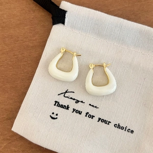 Détail de boucles d'oreilles en U dorées avec émail blanc sur un pochon cadeau