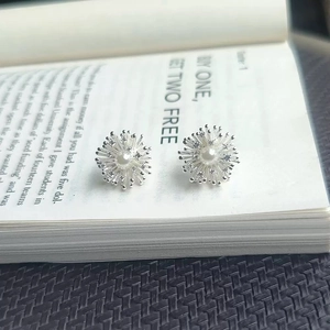 Silver fireworks flower stud earrings with central pearl and zircon on an open book