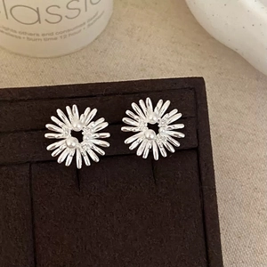 Silver daisy stud earrings with pearl centers on a dark velvet display stand