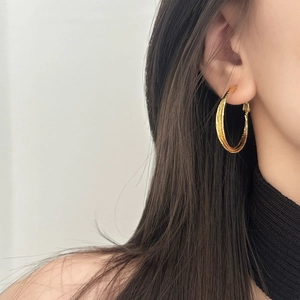 Detailansicht strukturierter goldener Mehrschicht-Creolen an einem Model in Schwarz