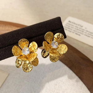 Detail of golden flower stud earrings with hammered petals and sparkling center zirconia