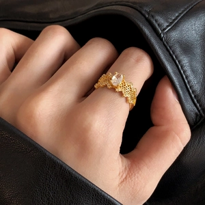 Detail of gold hollow mesh ring with oval crystal stone on model's hand and leather
