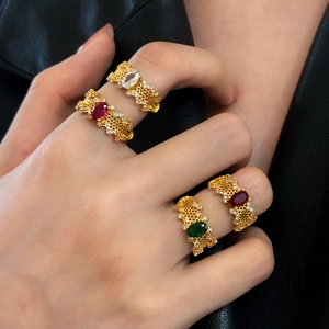 Detail of four gold hollow rings with red, green, and white oval gemstones set on models fingers