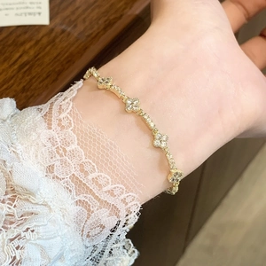 Bracelet trèfle doré élégant avec zircons blancs sur fond de dentelle blanche délicat