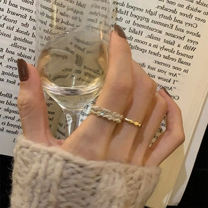 Close-up of a zircon-encrusted silver band and gold wavy ring on a model holding a glass