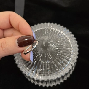 Detail showing wavy silver zircon ring held against a textured glass background
