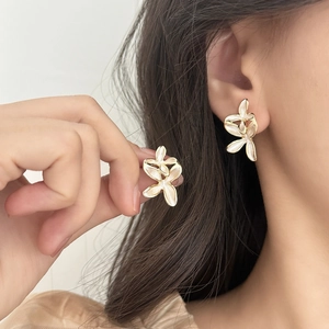 Close-up of elegant flower stud earrings with cream enamel and gold metal frame on ear