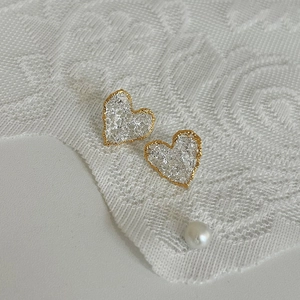 Close-up of heart-shaped gold lava earrings with silver lace texture on white fabric