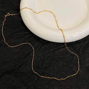 Elegant gold bead chain necklace displayed on black and white minimalist background