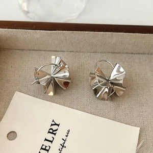Close-up of silver irregular pleated earrings displayed on a white textured jewelry tray