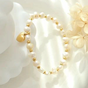 Elegantes Süßwasserperlenarmband mit goldenem Herzanhänger auf weißem Kunsttablett