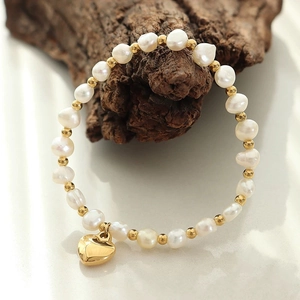 Elegantes Barock-Süßwasserperlenarmband mit goldenem Herzanhänger auf einem Naturholzast