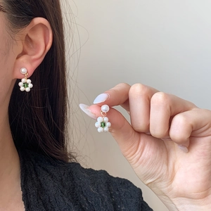 Elegant pearl flower earrings with green crystal center worn on model in soft light