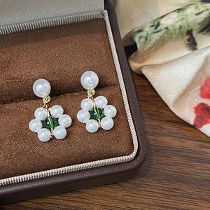 Macro view of floral pearl studs with green center bead on a luxury silk background