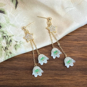 Détail de boucles d'oreilles franges dorées avec étoiles et muguet sur tissu floral