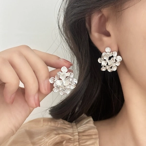 Silver flower cluster stud earrings with textured petals worn by a model in close-up