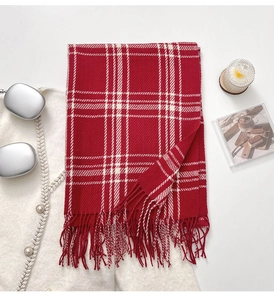 Flat lay of red and white plaid scarf with tassels alongside cozy winter accessories
