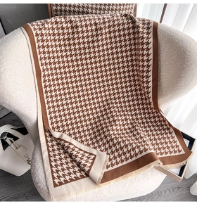 Dettaglio della morbida sciarpa pied de poule marrone con frange su una poltrona bianca