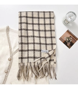 Detail of a thick plaid scarf with tassels and Cashmere Scarf label on a warm background