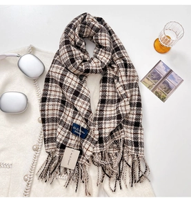 Detail of plaid scarf featuring fringed edges and woven brand label on soft cashmere-like fabric