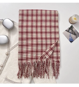Detailed view of red plaid scarf with tassels styled with headphones and candles