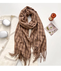 Détail d'une écharpe à carreaux café avec pompons, écouteurs et accessoires sur blanc
