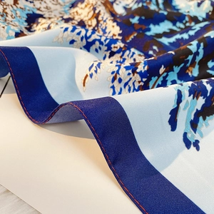Detailed view of floral silk scarf featuring navy blue borders and red contrast stitching