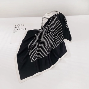 Détail d'un foulard en soie géométrique noir et blanc drapé sur un sac à main matelassé