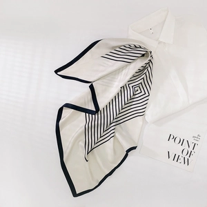 Détail d'un foulard en soie à rayures géométriques drapé sur une chemise blanche