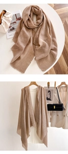 Detail of light beige scarf with short fringe texture shown on a white table and hanger
