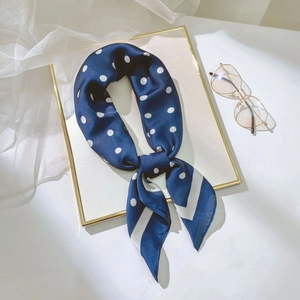 Gros plan d'un foulard en soie à pois bleu marine noué avec des lunettes vintage à côté