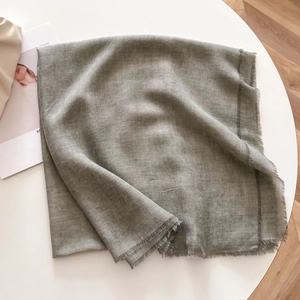 Close-up of olive green scarf with twill texture and fringe edges on a white table