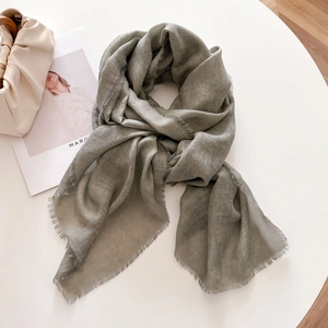 Detail of grey-green scarf with herringbone weave and fine fringe on a white table