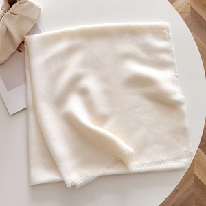 Detail of cream white summer shawl with delicate short tassels and soft texture