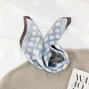 Detail of sky blue polka dot silk scarf draped over a beige knitted sweater