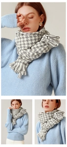 Detail of grey and white houndstooth scarf with fringe tassels worn on a knit sweater