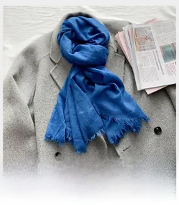 Détail d'une écharpe bleue en coton et lin avec franges sur un manteau en laine gris