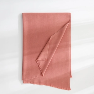 Detailed view of the soft fringed hem and fine texture of the warm pink cashmere shawl