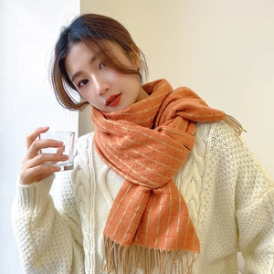Detail of warm orange cashmere-like scarf with thick knit texture and soft tassels