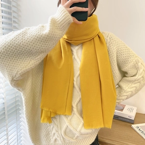 Vibrant yellow faux cashmere scarf with fringe details worn by a model in a cozy setting
