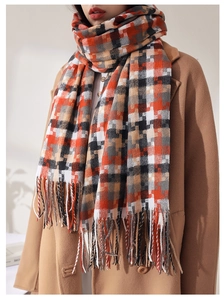 Détail d'une écharpe à carreaux avec pompons portée sur un manteau en laine beige