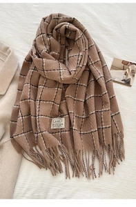 Close-up of brown plaid scarf with fringe tassels and woven brand label on white fabric
