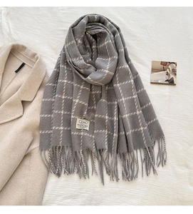 Detail of grey plaid scarf featuring soft fringe edges and a minimalist fabric brand label