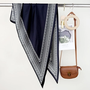 Dark blue silk scarf with white paisley pattern hung on a metal rack for autumn fashion
