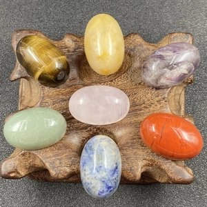 Close-up of seven egg-shaped natural gemstones on a carved wood base for meditation