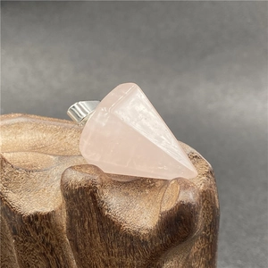 Macro shot of natural rose quartz hexagonal prism pendant on dark wood base